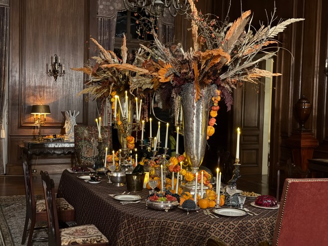 A beautifully set dining table adorned with elegant tableware, tall floral arrangements, and multiple candles, creating a warm and inviting atmosphere for a festive gathering.