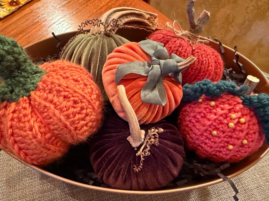 A collection of hand-crafted pumpkins displayed in a metallic bowl, featuring various colors and textures, including knitted and velvet designs.