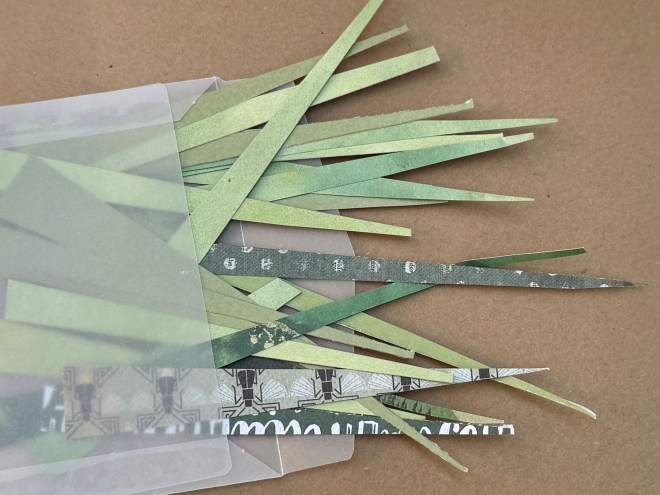 A collection of green paper strips and pieces arranged in a scattered manner on a brown surface, some peeking out from a transparent envelope.