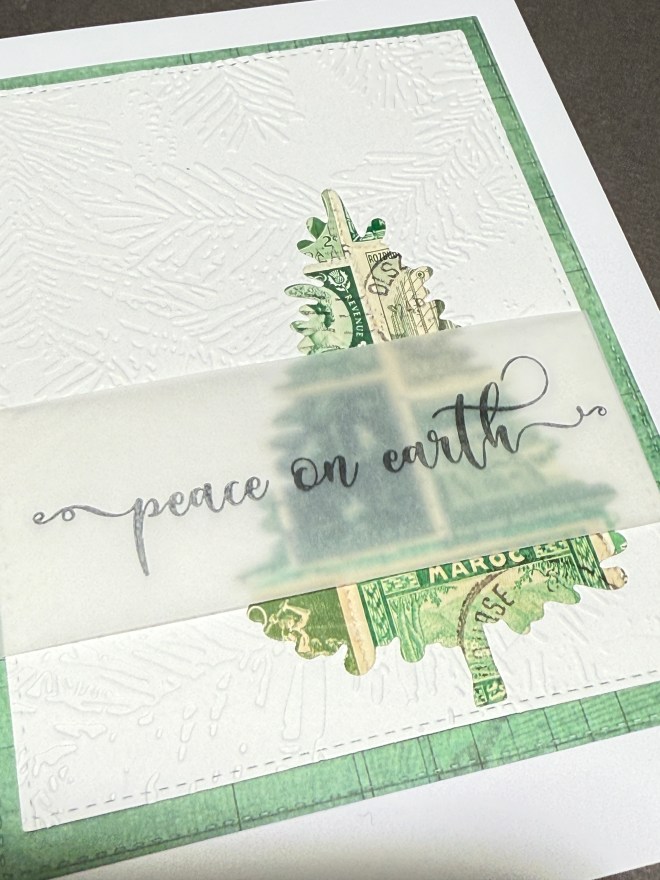 A Christmas card featuring an embossed white background, a decorative tree made from vintage postage stamps, and a translucent vellum overlay with the phrase 'peace on earth'.