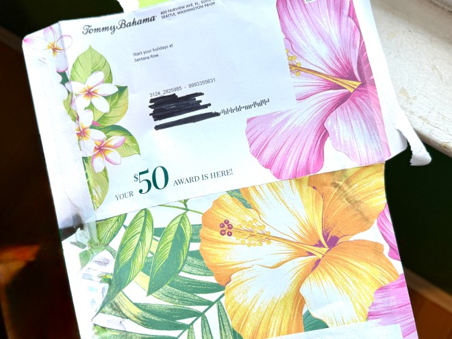 A partially opened envelope featuring tropical flower designs, with a message indicating a $50 award from Tommy Bahama.