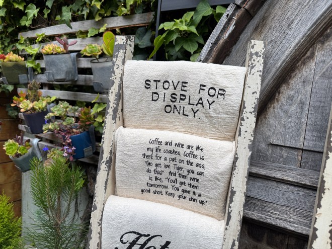 A decorative display featuring a sign that says 'STOVE FOR DISPLAY ONLY.' Below it, there is a humorous quote about coffee and wine, emphasizing their importance in life.