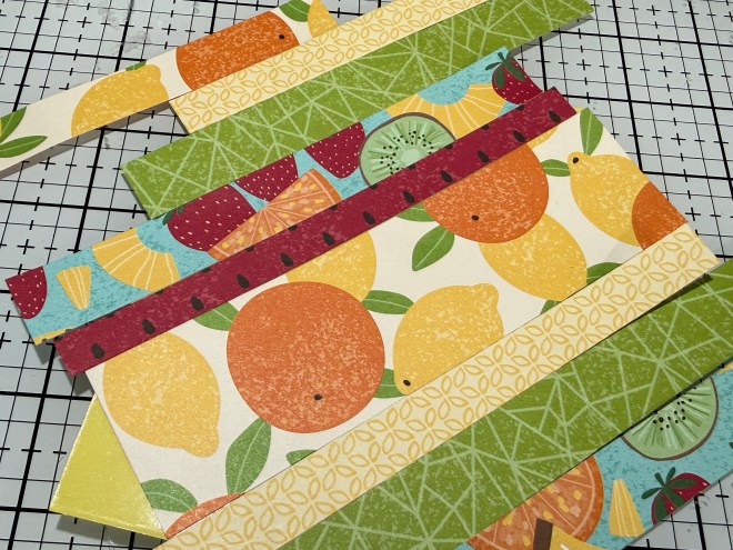 Colorful patterned paper strips featuring illustrations of various fruits, including lemons, oranges, and kiwis, arranged on a grid background.