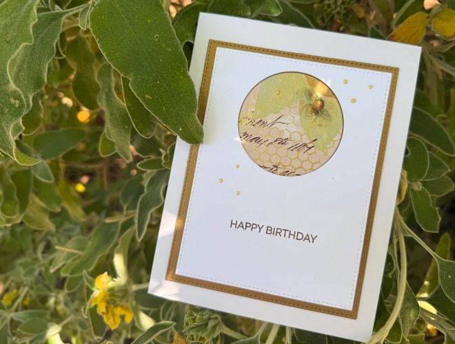 A birthday card with a circular design featuring honeycomb and a bee, set against a background of green foliage.