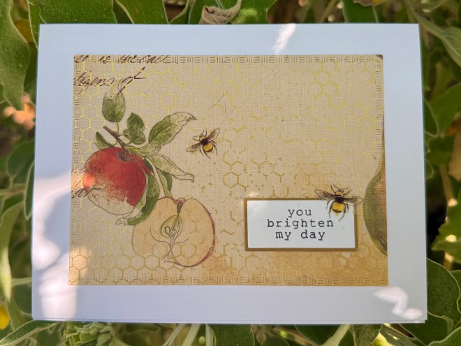 A decorative card featuring an illustration of apples and bees with the text 'you brighten my day'.