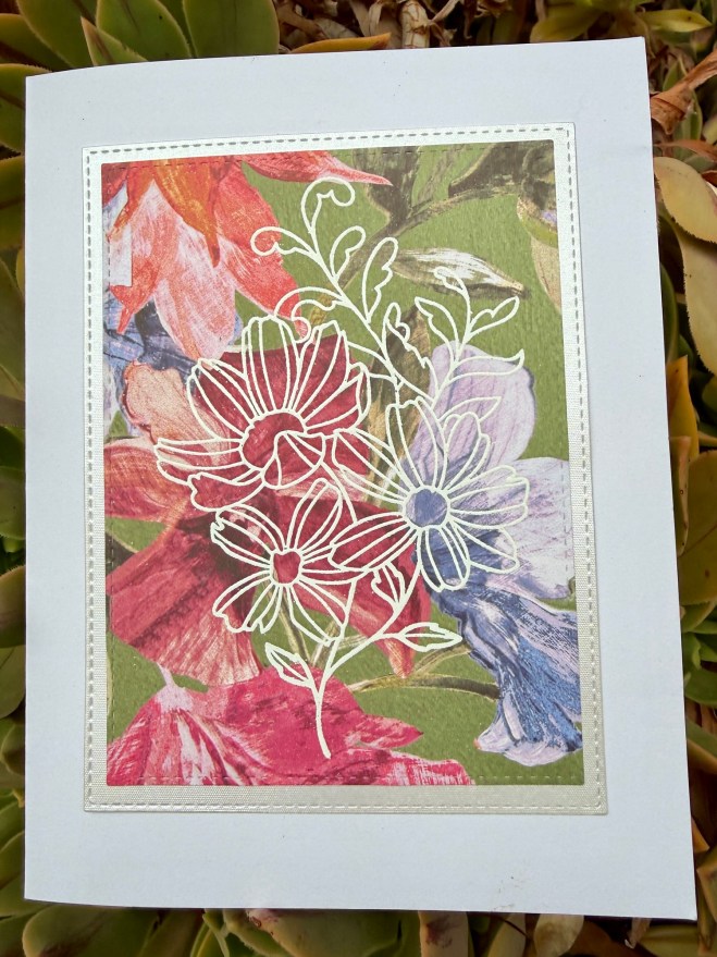 A floral card featuring a white outlined drawing of flowers over a colorful background of various vibrant flowers.