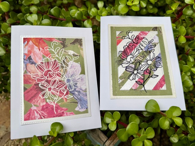Two handmade greeting cards featuring floral designs, each with a different color palette and outline styles, placed on a backdrop of green foliage.